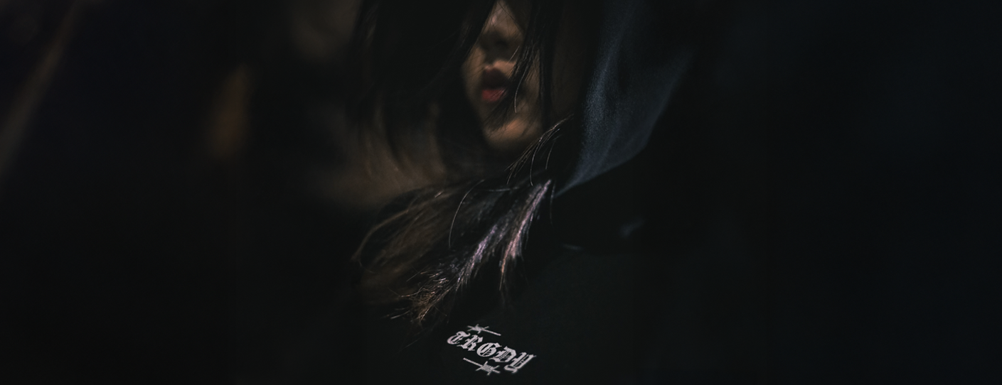 Dark-themed image with a person wearing a hoodie featuring a brand logo.slider_item_Nqa9eL