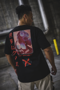 A person standing in a dark industrial setting wearing a black oversize tee with rear graphic of a reddish colored image of a girl in a gas mask doing a middle finger with orange/red text below stating 